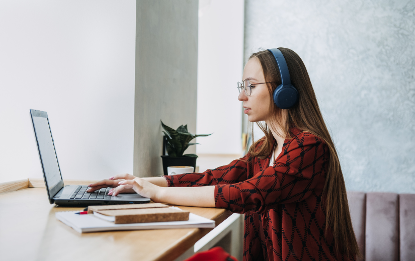 Woman working on a laptop with headphones, focusing on side hustle ideas for earning income online from a cozy workspace.